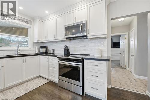 Kitchen with stainless steel appliances, white cabinets, and dark wood-style flooring - 473 Mohawk Road W, Hamilton, ON 