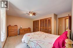 Carpeted bedroom featuring two sets of bi-fold louvered closet doors, a sloped ceiling, and a ceiling fan with integrated lighting - 