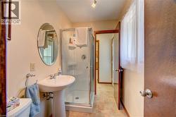 Bathroom featuring a pedestal sink, oval mirror, glass-enclosed shower, and neutral tile flooring - 