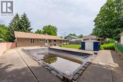 Concrete patio with an in-ground swimming pool, featuring a blue and white utility shed, and a stone-clad exterior on the single-story residence - 