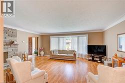 Spacious living area featuring wood-finish flooring, a stone-faced fireplace with a wood mantel, crown molding, a bay window, and a paneled entry door - 