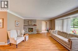 Spacious living area featuring wood-finish flooring, a stone-clad fireplace, a large bay window, and crown molding - 