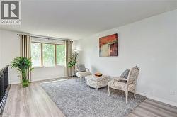 Bright upper-level space featuring large windows, light wood-finish flooring, white walls, a black metal railing, and a gray area rug - 