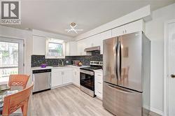Kitchen featuring white cabinetry, stainless steel appliances, a dark mosaic tile backsplash, light wood-finish flooring, and a window above the sink - 