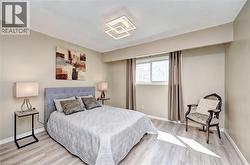 Bedroom featuring light wood-finish flooring, a contemporary ceiling light fixture, and a window with drapes - 