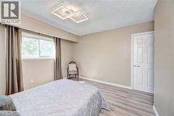 Spacious room featuring wood-finish flooring, a large window, contemporary ceiling light fixture, panel interior door, and neutral wall tones - 