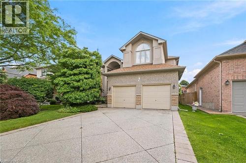 Brick and stucco exterior featuring an arched window, a two-car garage, concrete driveway, and mature landscaping - 207 Valridge Drive, Ancaster, ON - Outdoor