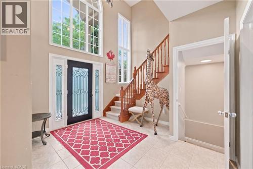 Foyer featuring a grand entry door with decorative glass inserts and sidelights, a two-story arched window, a staircase with wood railings, and tile flooring - 207 Valridge Drive, Ancaster, ON - Indoor Photo Showing Other Room