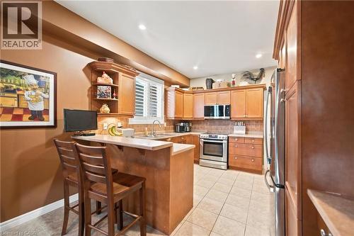 Kitchen featuring wood-finish cabinetry, stainless steel appliances, tiled backsplash, and a breakfast bar with a light-toned countertop - 207 Valridge Drive, Ancaster, ON - Indoor Photo Showing Kitchen