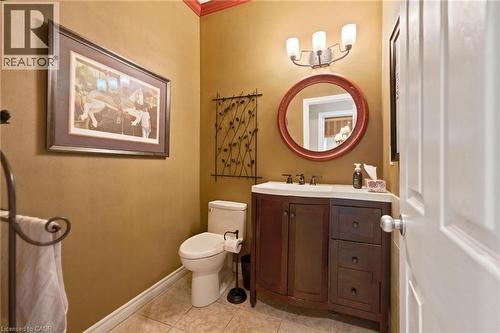 Bathroom vanity featuring a dark wood-finish cabinet with a white countertop and sink, complemented by a round framed mirror and a three-light fixture - 207 Valridge Drive, Ancaster, ON - Indoor Photo Showing Bathroom