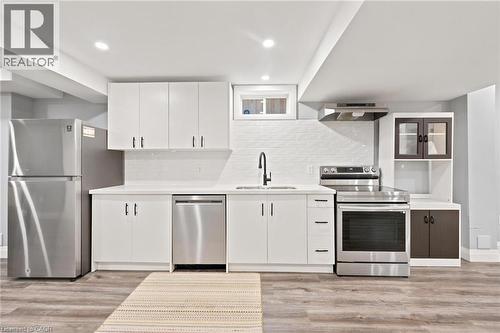 Kitchen featuring stainless steel appliances, white cabinetry, solid surface countertops, a white subway tile backsplash, and wood-finish flooring - 207 Valridge Drive, Ancaster, ON - Indoor Photo Showing Kitchen