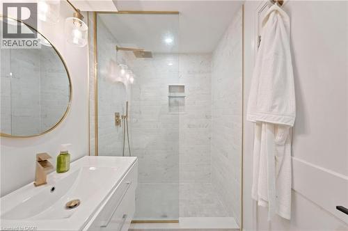 Modern bathroom featuring a frameless glass shower enclosure with gold-finish fixtures, marble-patterned tile, and a built-in shower niche - 207 Valridge Drive, Ancaster, ON - Indoor Photo Showing Bathroom