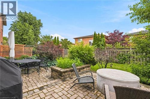 Paver patio with a stone planter, dark metal fencing, and mature landscaping - 207 Valridge Drive, Ancaster, ON - Outdoor