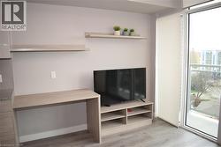 Open-concept living space with wood-finish flooring, featuring a built-in desk, floating shelving, and a media console - 