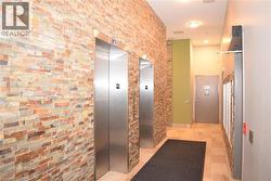 Entry foyer featuring two stainless steel elevators, stacked stone accent walls, recessed lighting, and tile flooring - 