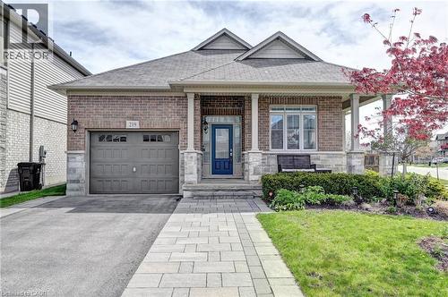 Brick and stone facade bungalow featuring a covered front porch with columns, an asphalt driveway, a paver stone walkway, and a single-car garage with an overhead door - 219 Falconridge Drive, Kitchener, ON - Outdoor With Facade