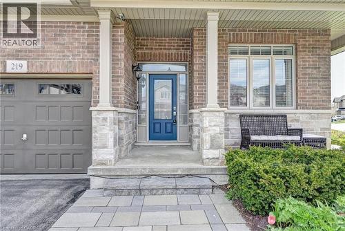 Brick and stone facade featuring a prominent blue entry door, an integrated garage with transom windows, and a covered porch with architectural columns - 219 Falconridge Drive, Kitchener, ON - Outdoor