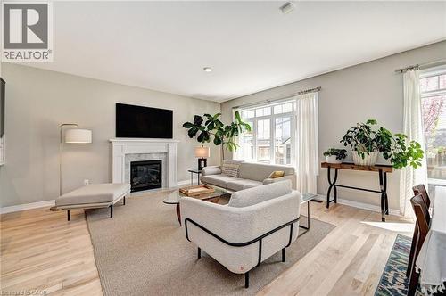 Living area featuring light wood-finish flooring, a white mantel fireplace with a dark stone surround, and multiple large windows with white trim - 219 Falconridge Drive, Kitchener, ON - Indoor Photo Showing Living Room With Fireplace