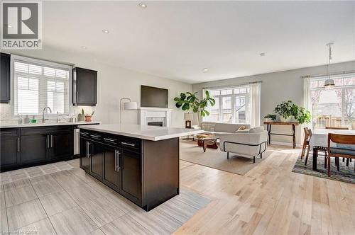 Open-concept living space featuring a kitchen island, dark wood-finish cabinetry, light wood-finish flooring, a white fireplace with mantle, and white window blinds - 219 Falconridge Drive, Kitchener, ON - Indoor