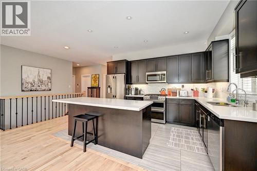 Modern kitchen featuring dark wood-finish cabinetry, stainless steel appliances, white countertops, and a full tile backsplash - 219 Falconridge Drive, Kitchener, ON - Indoor Photo Showing Kitchen With Upgraded Kitchen