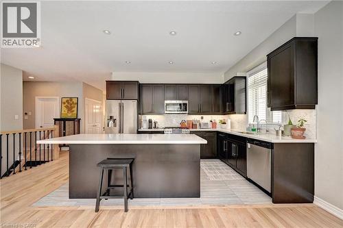 Modern kitchen featuring dark wood cabinetry, stainless steel appliances, a white solid surface countertop, and a center island with bar seating - 219 Falconridge Drive, Kitchener, ON - Indoor Photo Showing Kitchen With Upgraded Kitchen