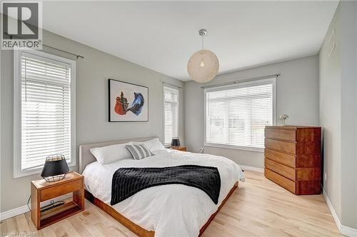 Bright bedroom featuring light wood-finish flooring, multiple windows with blinds, a modern ceiling light fixture, and neutral wall paint - 219 Falconridge Drive, Kitchener, ON - Indoor Photo Showing Bedroom