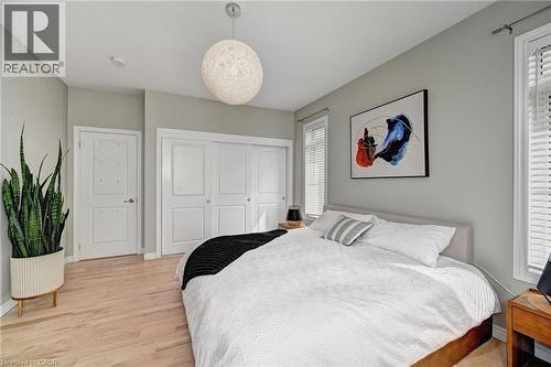 Bedroom featuring light wood-finish flooring, two large windows with blinds, a modern spherical pendant light fixture, and white bi-fold closet doors - 219 Falconridge Drive, Kitchener, ON - Indoor Photo Showing Bedroom