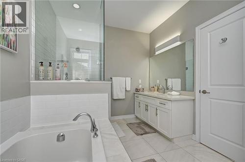 Modern bathroom featuring a built-in tub with white subway tile surround, a glass-enclosed shower, a double vanity with white cabinetry, a large mirror, and neutral-toned floor tiling - 219 Falconridge Drive, Kitchener, ON - Indoor Photo Showing Bathroom