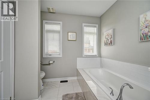 Soaking tub with a polished chrome faucet, white subway tile surround, and two windows with horizontal blinds - 219 Falconridge Drive, Kitchener, ON - Indoor Photo Showing Bathroom