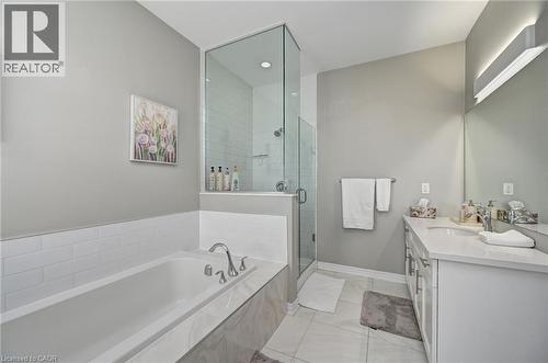 Full bathroom featuring a framed glass shower enclosure, a white tiled bathtub surround, a single vanity with a white countertop and undermount sink, a large mirror, and light-toned floor tiling - 219 Falconridge Drive, Kitchener, ON - Indoor Photo Showing Bathroom