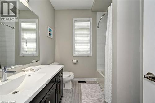 Bathroom featuring a white subway tile tub surround, dark wood-finish vanity with a white countertop, chrome faucet, and wood-finish flooring - 219 Falconridge Drive, Kitchener, ON - Indoor Photo Showing Bathroom