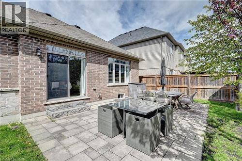Expansive paver patio with a brick and stone exterior, featuring a sliding glass door entry and a private wood fence - 219 Falconridge Drive, Kitchener, ON - Outdoor With Deck Patio Veranda