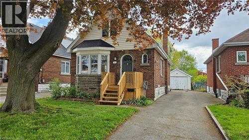 Brick and siding residence featuring a bay window with stone accents, a new wood deck, and a paved driveway leading to a detached garage - 75 Barons Avenue S, Hamilton, ON - Outdoor