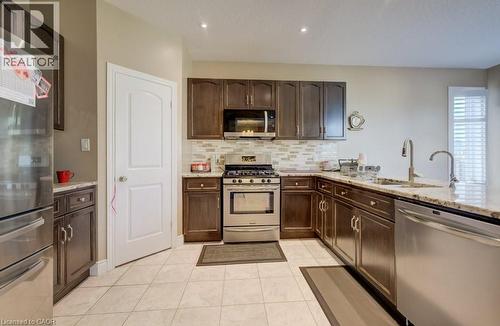 Modern kitchen featuring dark wood-finish cabinetry, stainless steel appliances, a tile backsplash, light-toned countertops, and recessed lighting - 331 Westpark Crescent Unit# Upper, Waterloo, ON - Indoor Photo Showing Kitchen With Double Sink