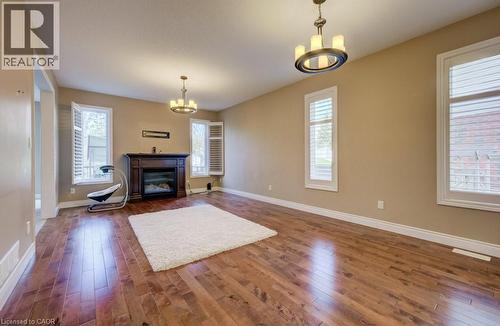 Spacious room featuring wood-finish flooring, a dark wood fireplace with an electric insert, and multiple windows with white plantation shutters - 331 Westpark Crescent Unit# Upper, Waterloo, ON - Indoor Photo Showing Living Room With Fireplace