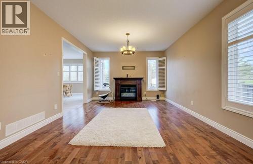 Spacious room featuring rich wood-finish flooring, a central fireplace with a dark wood mantel, and multiple windows fitted with white plantation shutters - 331 Westpark Crescent Unit# Upper, Waterloo, ON - Indoor Photo Showing Living Room With Fireplace