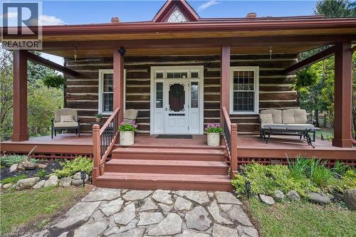 Rustic log cabin exterior featuring a covered front porch, white-paneled front door, stone pathway, red-stained steps, and latticework foundation skirting - 630 Robert Ferrie Drive, Kitchener, ON - Outdoor With Deck Patio Veranda