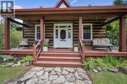 Rustic log cabin exterior featuring a covered front porch, white-paneled front door, stone pathway, red-stained steps, and latticework foundation skirting - 