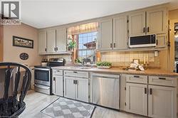 Kitchen featuring light-toned cabinetry, stainless steel appliances, a window above the sink, a tiled backsplash, and wood-finish flooring - 