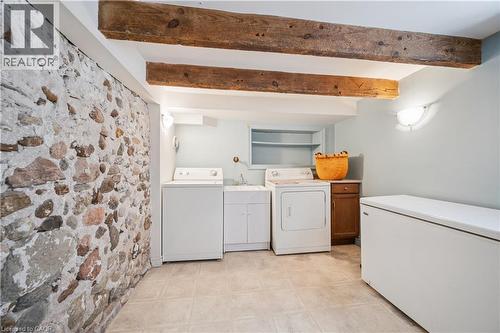 Laundry area featuring an exposed stone wall, wood-finish ceiling beams, and tile flooring - 630 Robert Ferrie Drive, Kitchener, ON - Indoor Photo Showing Laundry Room