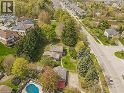 Aerial view showcasing the property's irregular-shaped swimming pool, surrounded by mature trees and a fenced perimeter - 