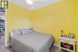 Compact bedroom featuring vibrant yellow walls, light wood-finish flooring, and a ceiling fan with integrated lighting - 