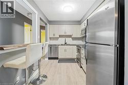Modern kitchen featuring stainless steel appliances, light wood-finish flooring, white shaker-style cabinetry, and a subway tile backsplash - 