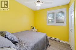 Bright room featuring a window with white shutters, wood-finish flooring, a ceiling fan, and a white paneled door - 