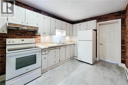 Kitchen with white appliances, brick wall, light countertops, under cabinet range hood, and light marble finish floors - 156 Park Row S, Hamilton, ON - Indoor Photo Showing Kitchen