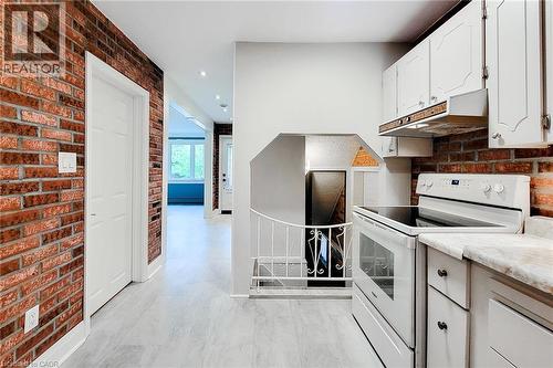 Kitchen with brick wall, white electric range, under cabinet range hood, white cabinets, and recessed lighting - 156 Park Row S, Hamilton, ON - Indoor Photo Showing Kitchen
