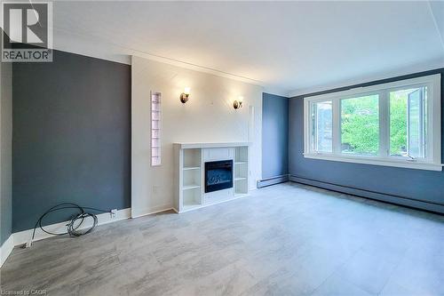 Unfurnished living room featuring healthy amount of natural light and a glass covered electric fireplace framed by glass block window accents. - 156 Park Row S, Hamilton, ON - Indoor With Fireplace