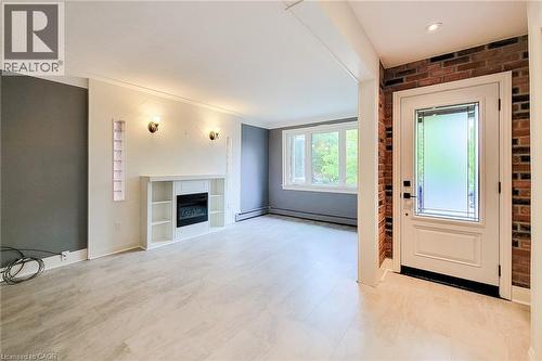 Foyer entrance with a glass covered fireplace, brick wall, and light flooring. - 156 Park Row S, Hamilton, ON - Indoor With Fireplace