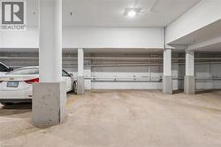 Concrete parking garage with exposed overhead piping, white support columns, and overhead lighting - 