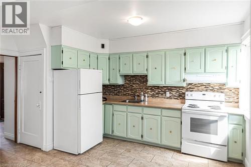 Kitchen featuring light green cabinetry, a mosaic tile backsplash, and light-toned countertops - 114 Weir Street N, Hamilton, ON - Indoor Photo Showing Kitchen